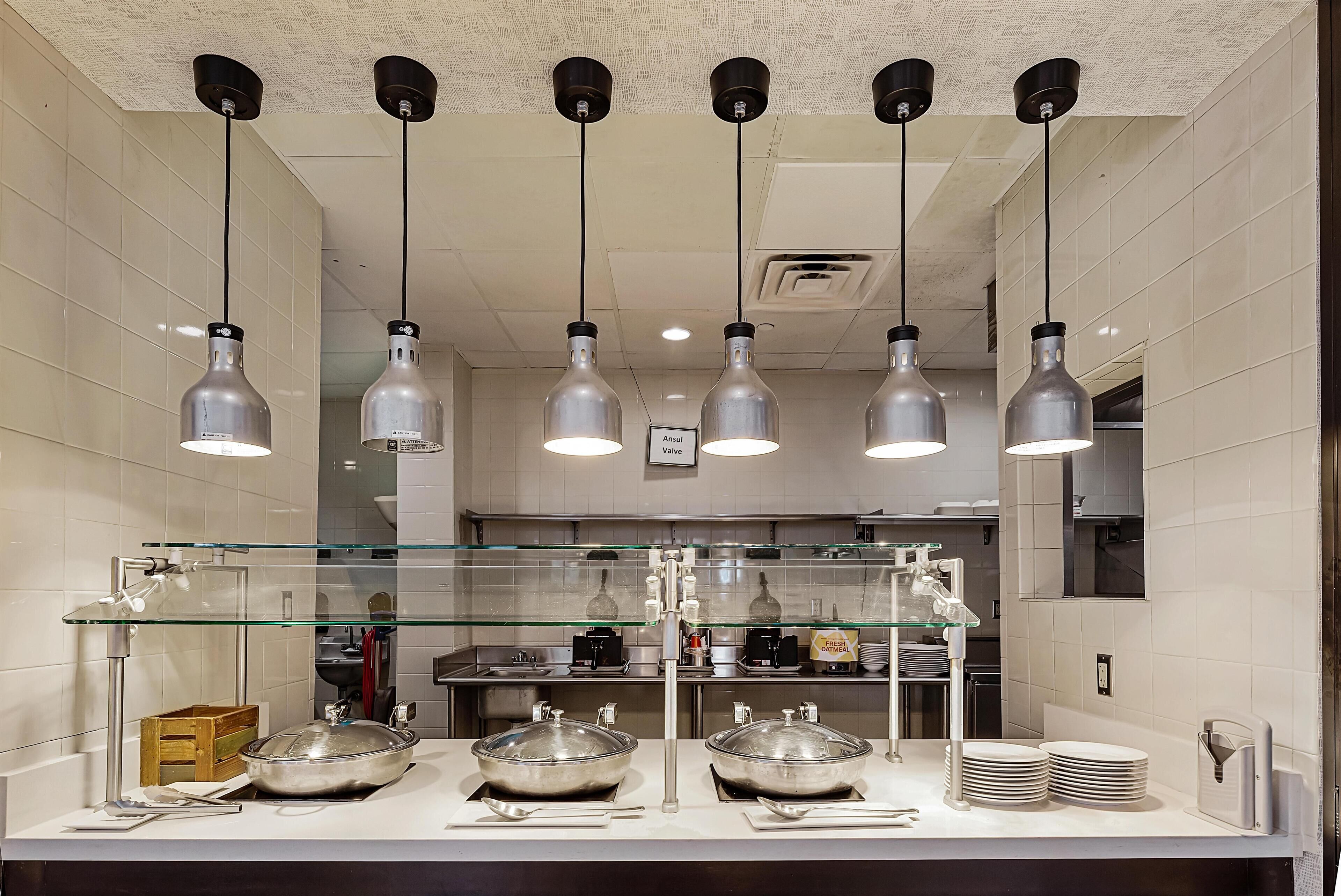 Une cuisine moderne dotée d’appareils électroménagers en acier inoxydable, d’une cloison en verre et de plusieurs luminaires suspendus.