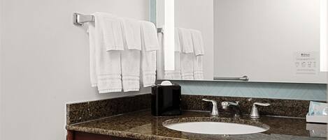 A bathroom with a sink, mirror, towel rack, and trash can.