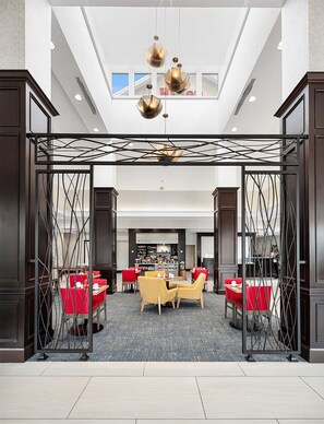 A spacious lobby with a central seating area, a The Shop, and a view of the sky through the ceiling. - Hilton Garden Inn New Braunfels (New Braunfels)