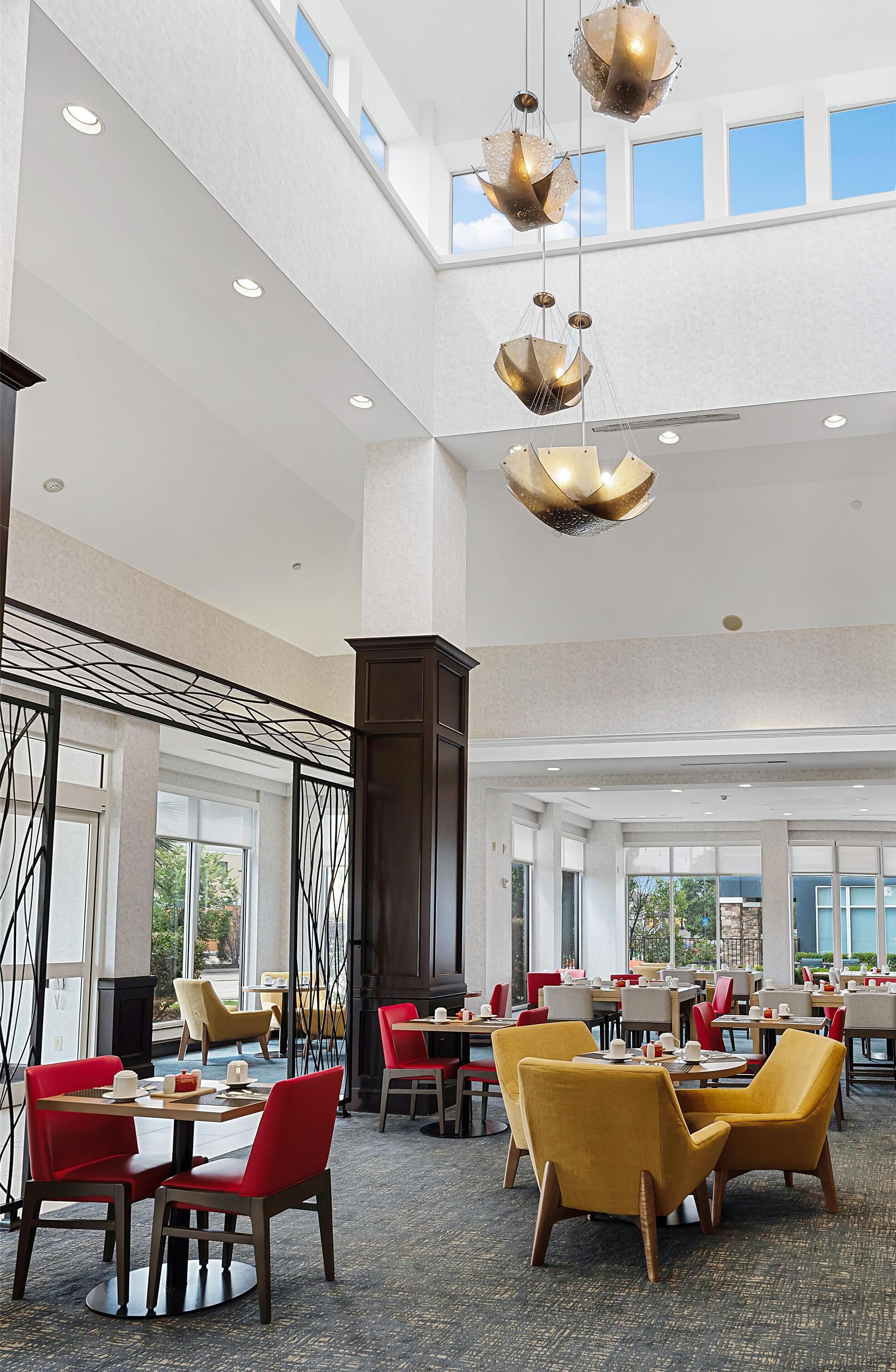 Un amplio vestíbulo de hotel con techos altos, modernos candelabros y una mezcla de sillas rojas y amarillas.