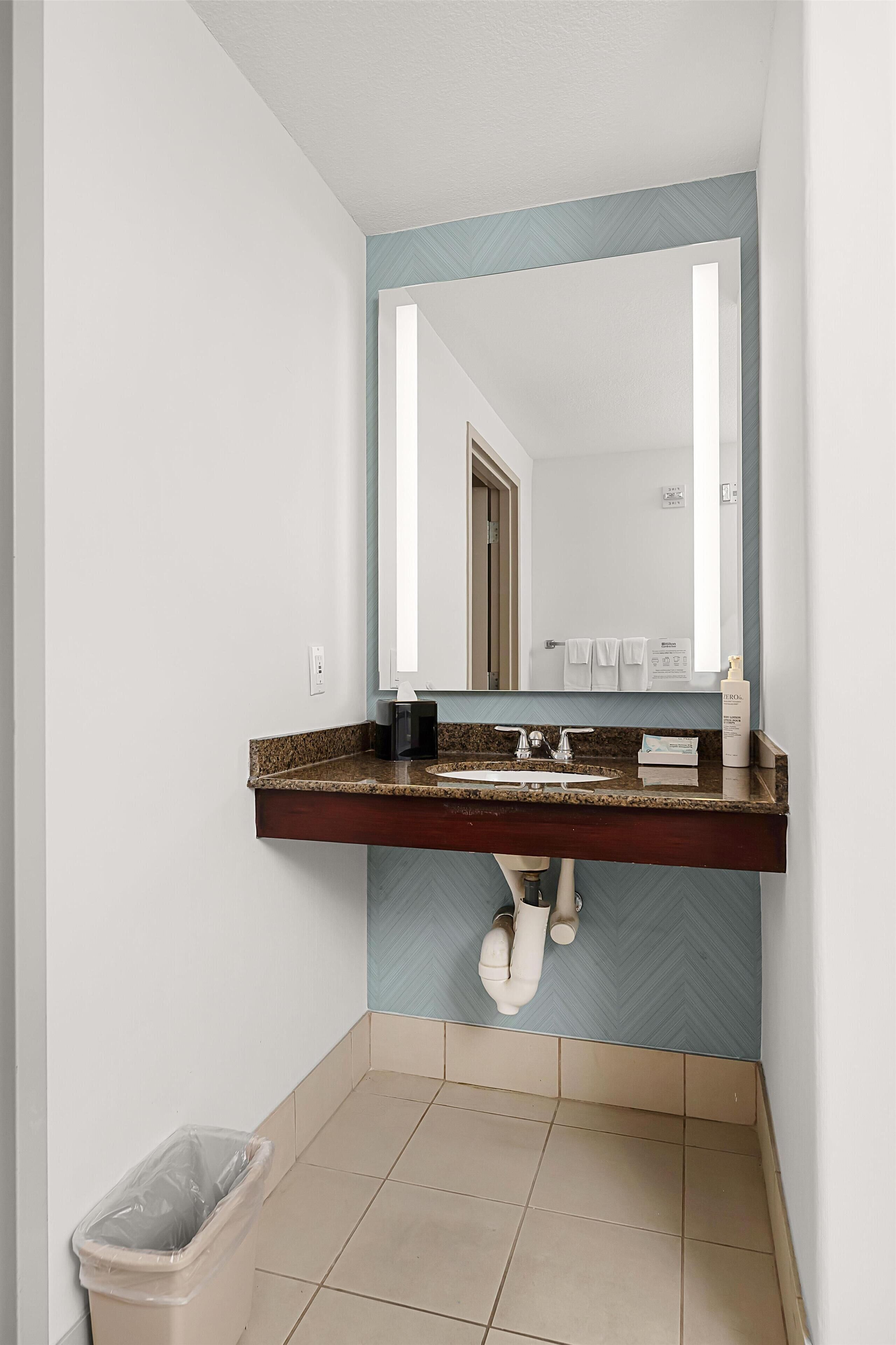 Une salle de bain avec un comptoir en granit, un miroir, un lavabo et une poubelle.