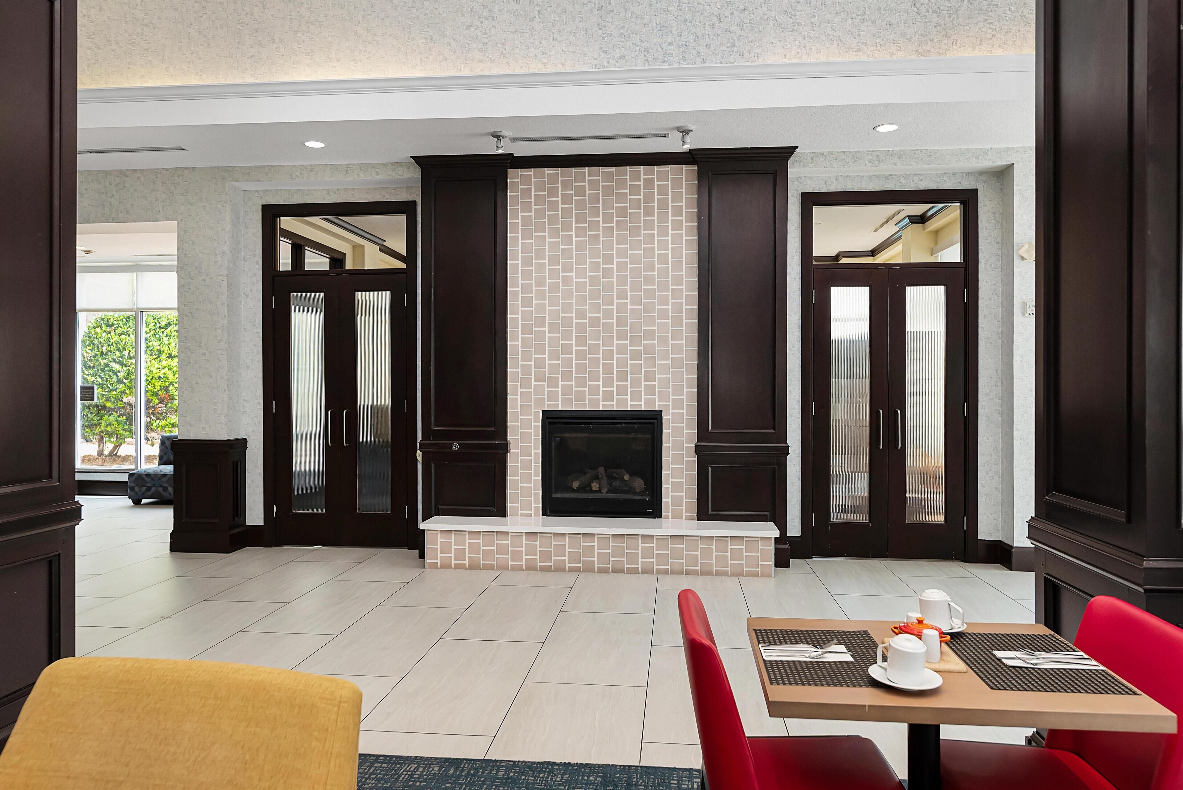 A hotel lobby with a fireplace, dark wooden doors, and a seating area with a table set for two.