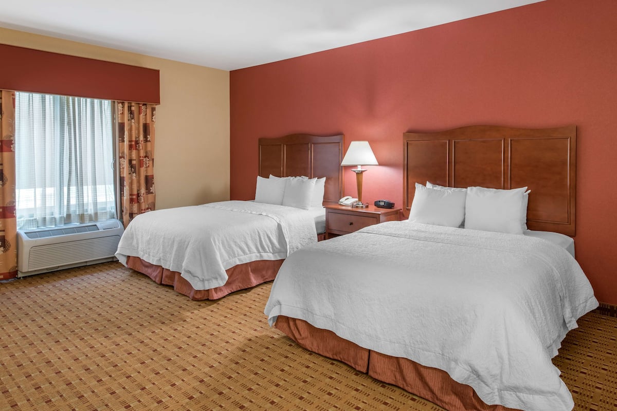 Quarto de hotel com duas camas, uma mesa de cabeceira, um abajur e uma janela com cortinas.