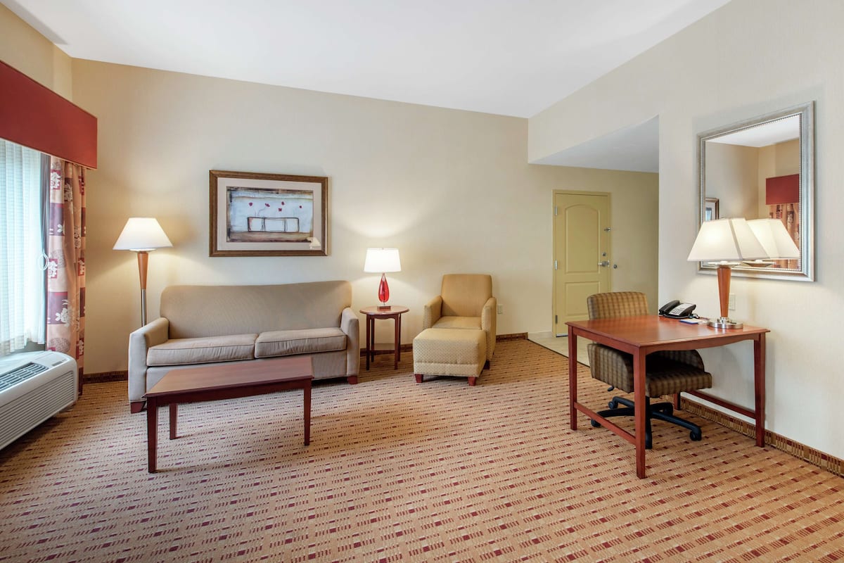 Quarto de hotel com sofá, poltrona, escrivaninha e luminárias.