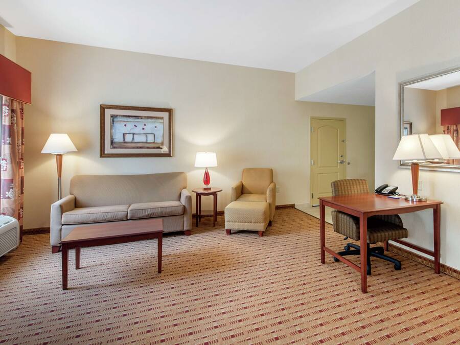 A hotel room with a sofa, armchair, desk, and lamps.