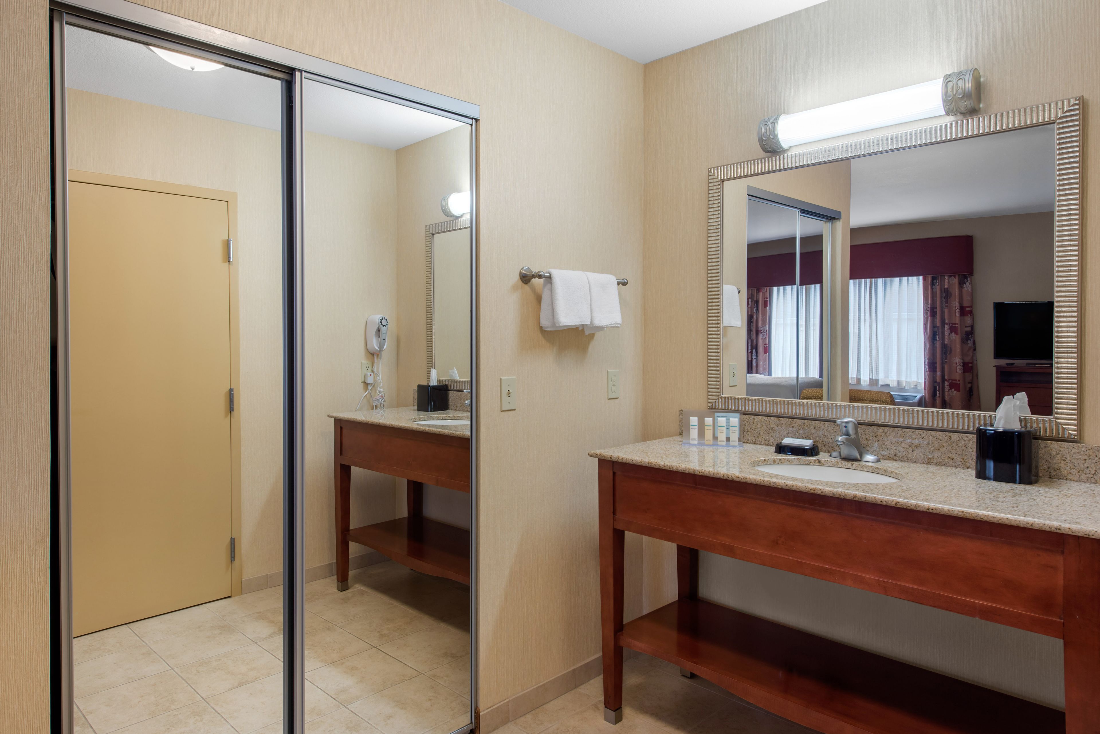 A hotel bathroom with a large mirror, a sink, a towel rack, and a door.