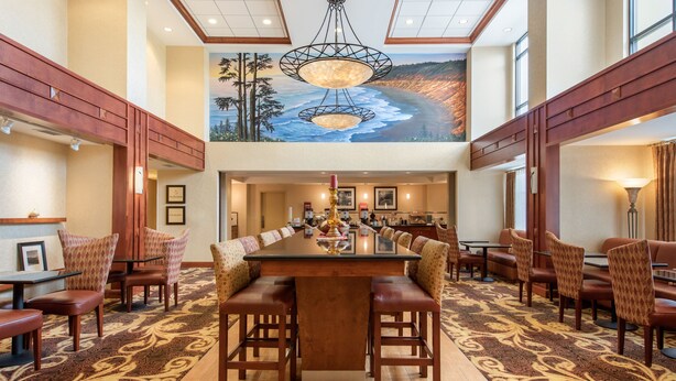 A spacious dining area with a long table and multiple chairs, a chandelier, and a mural of a beach scene on the wall. - Hampton Inn & Suites Arcata (Arcata)
