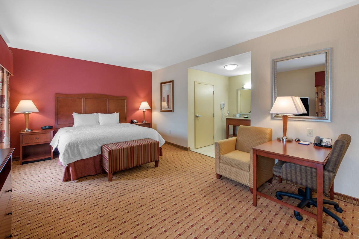 Quarto de hotel com cama, mesas de cabeceira, escrivaninha com cadeira, espelho e porta que dá para outro quarto.