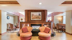 A lobby with two armchairs, a fireplace, a framed picture above the fireplace, and a dining area in the background. - Hampton Inn & Suites Arcata (Arcata)