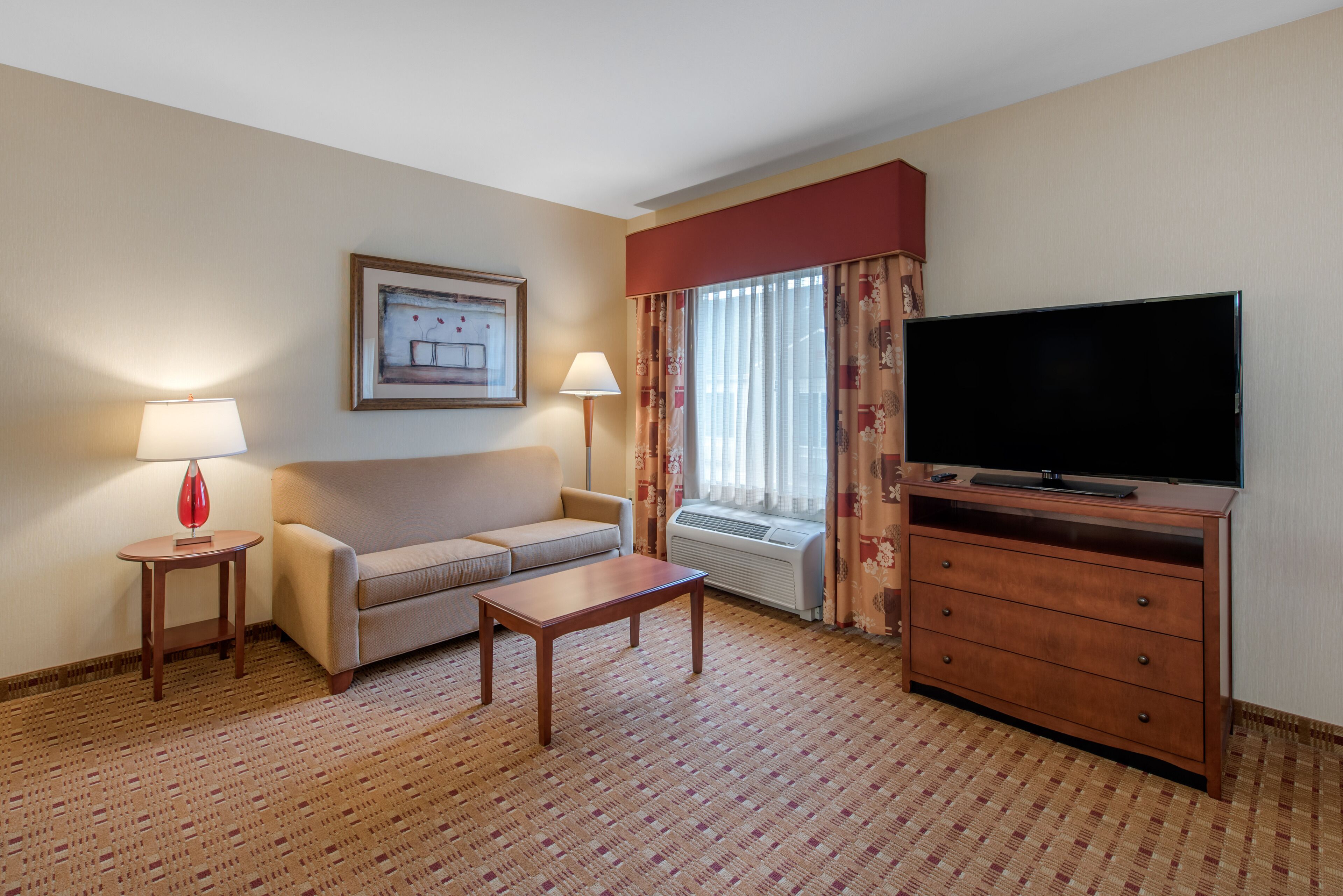 Una camera d'albergo con un divano, un tavolino, una TV, una lampada e un quadro appeso al muro.