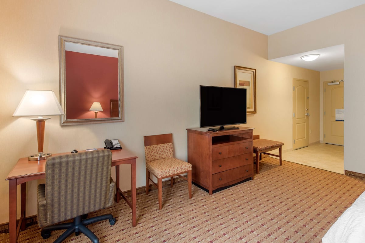 Quarto de hotel com escrivaninha, cadeira, televisão, cômoda e cama.