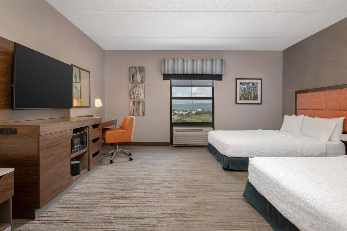 Une chambre d’hôtel équipée d’un lit, d’un bureau avec un téléviseur à écran plat, d’une chaise, d’une fenêtre donnant sur un paysage agréable et d’un appareil de climatisation.