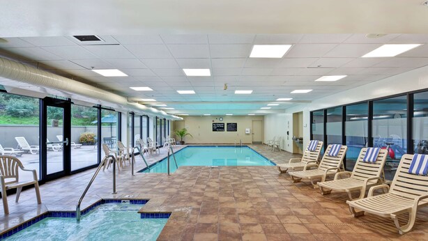 Una piscina interior con suelo de baldosas, sillones de descanso y grandes ventanales con vistas al exterior.