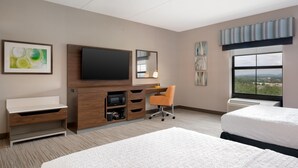 Habitación de hotel con cama, escritorio con silla, televisión de pantalla plana, espejo, obras de arte en las paredes y ventana con vistas.