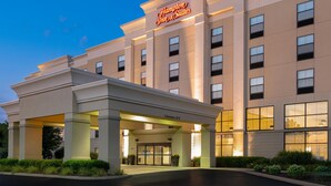 Un hotel Hampton Inn & Suites con entrada despejada, un letrero sobre la entrada y un cielo claro al fondo.