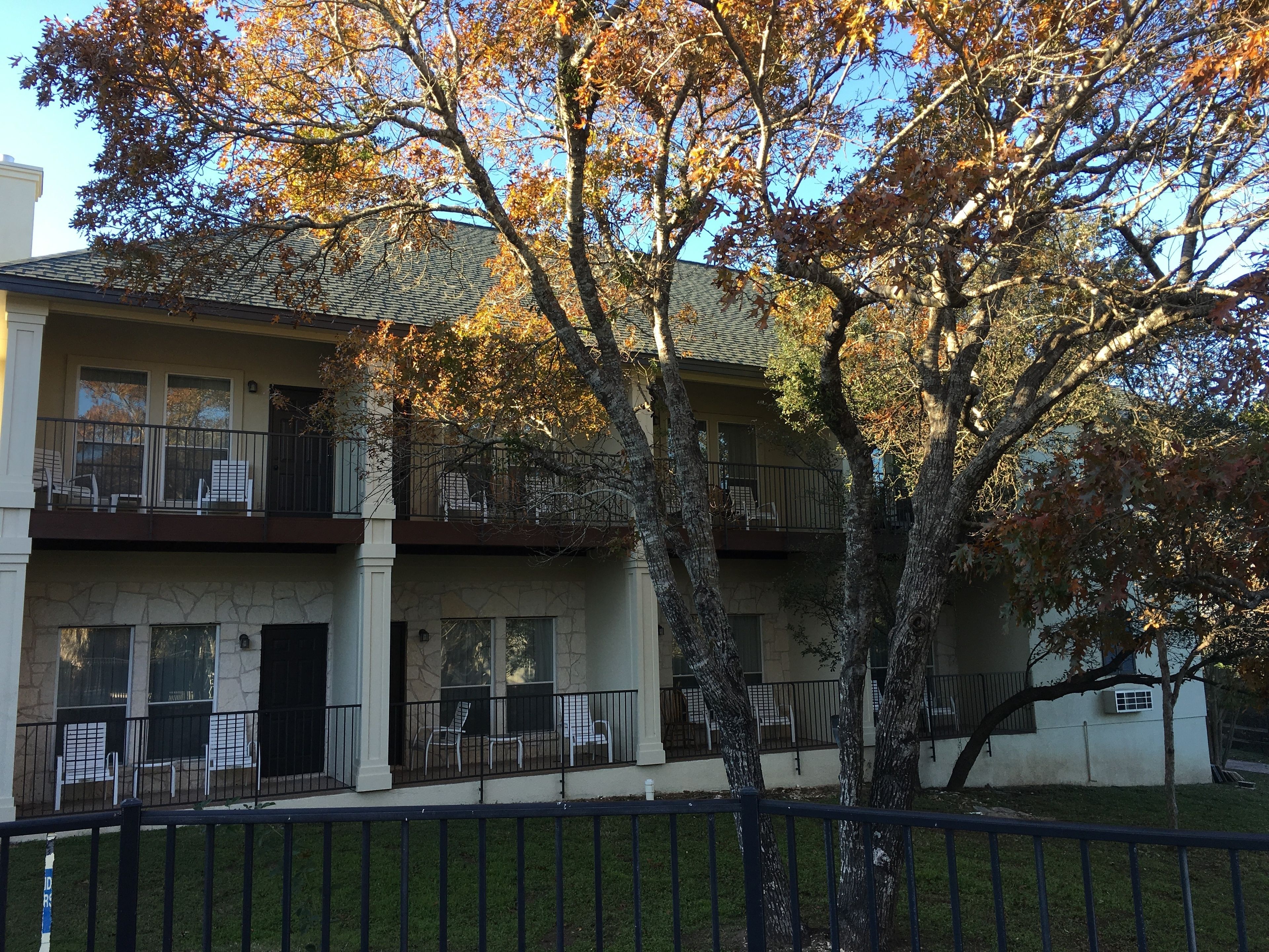 Edifici de dues plantes amb façana de pedra, diversos balcons i un arbre al primer pla.