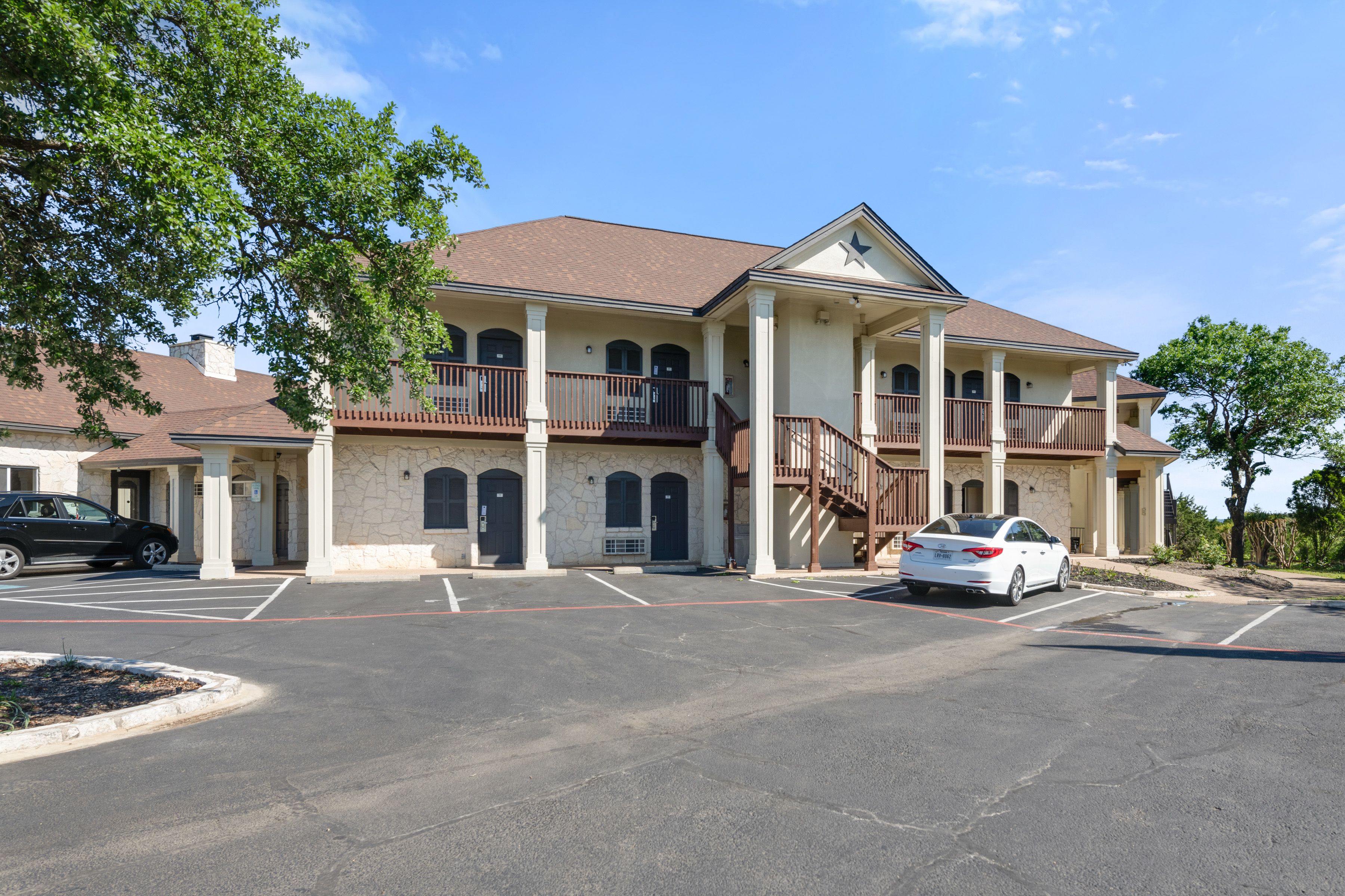 A two-story building with a stone facade, multiple balconies, and a parking lot.