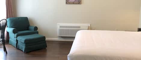 A bedroom with a bed, a chair, a heater, and a ceiling fan.