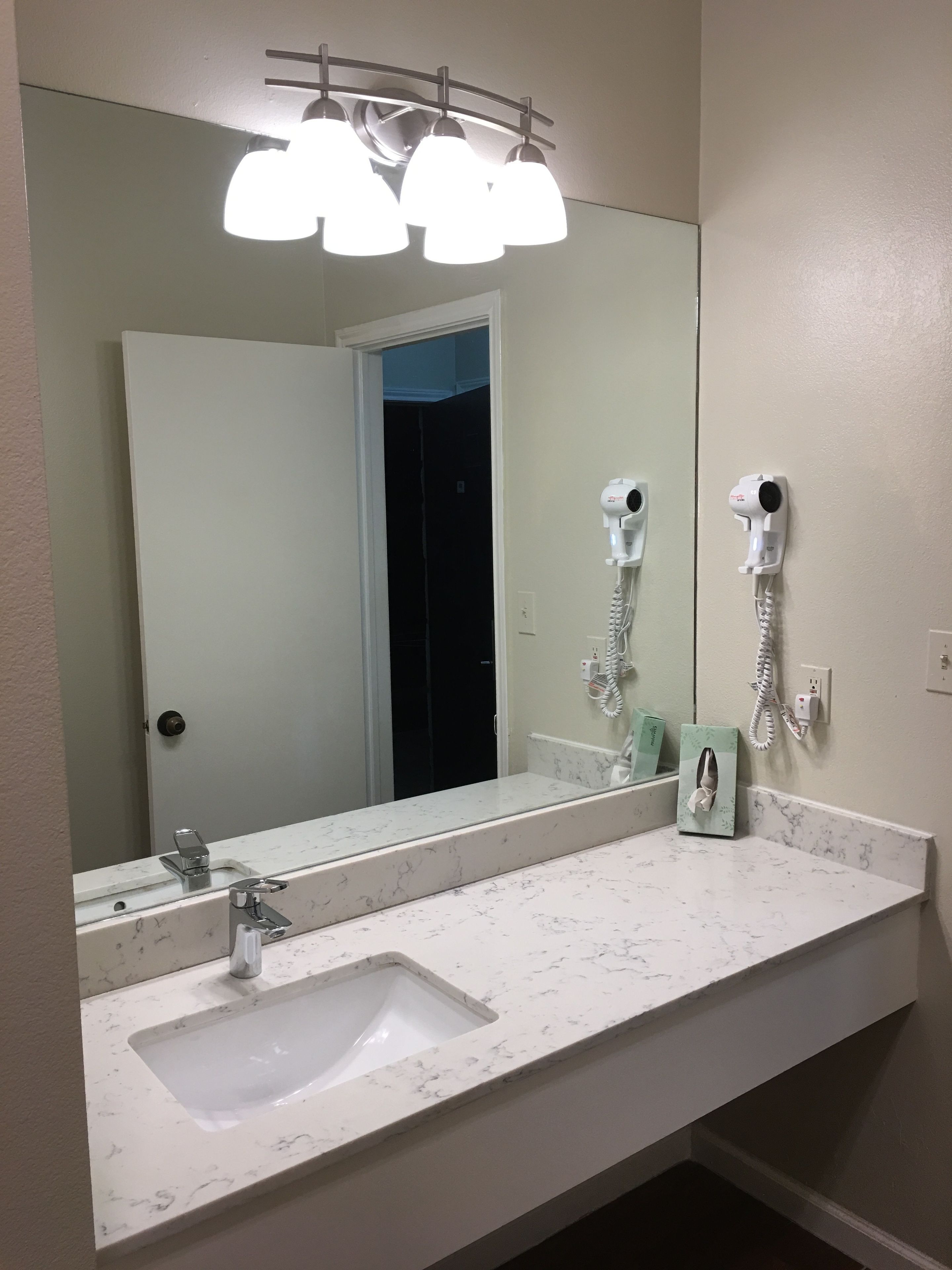 A bathroom with a large mirror, a sink, and two hair dryers mounted on the wall.