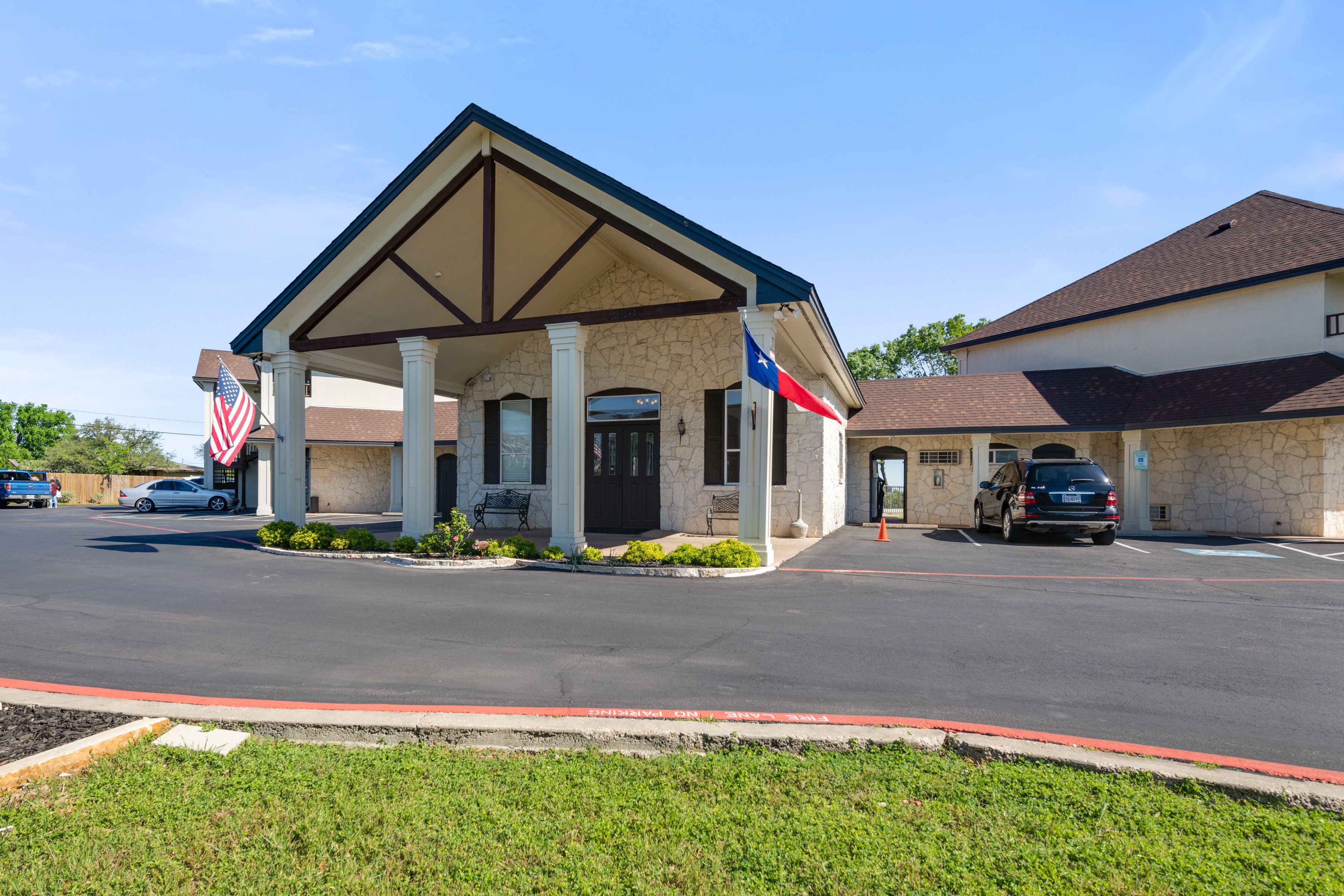A building with a covered entrance, two flags, and a parking lot.