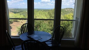 A room with a table and chairs facing a large window with a view of a green landscape and a clear sky. - Mountain Star Lodge (Austin)