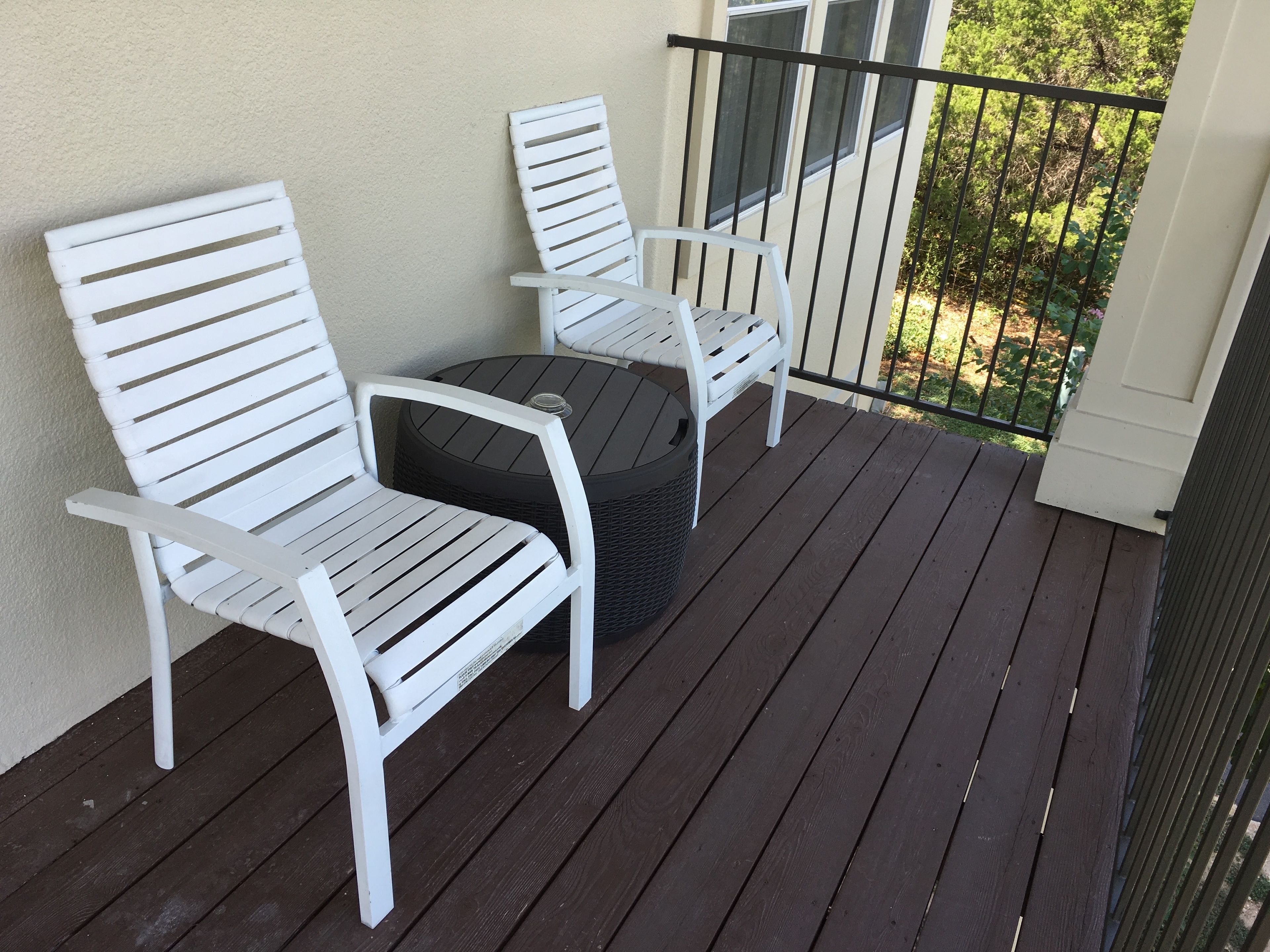 Een balkon met twee witte stoelen en een ronde tafel.
