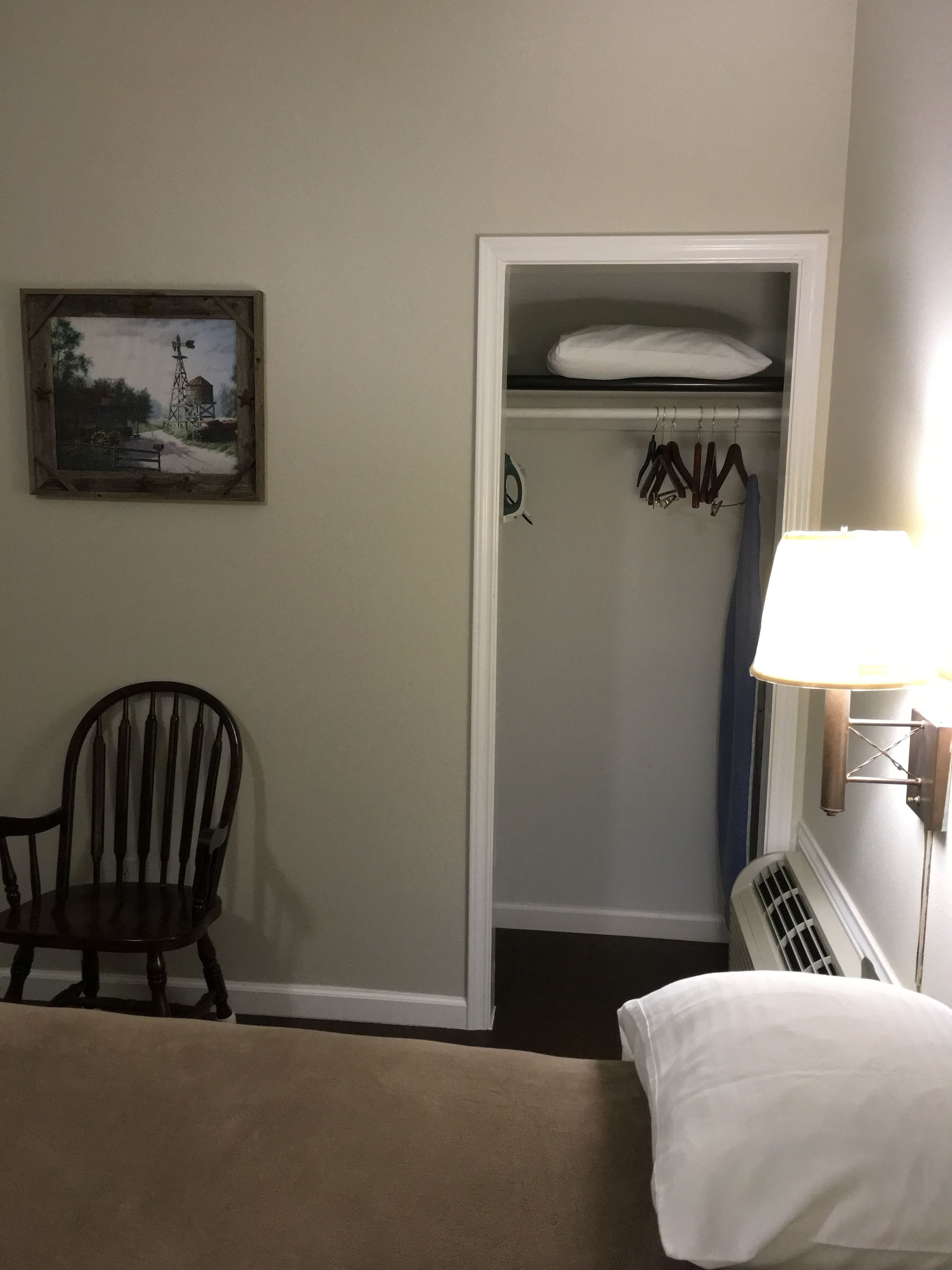 A hotel room with a bed, a chair, a wardrobe, and a painting on the wall.