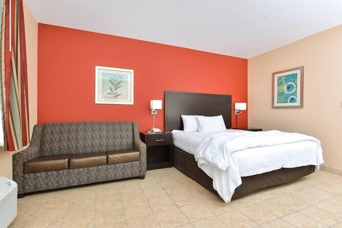 A hotel room with a bed, a sofa, two bedside tables, and two wall-mounted lamps.