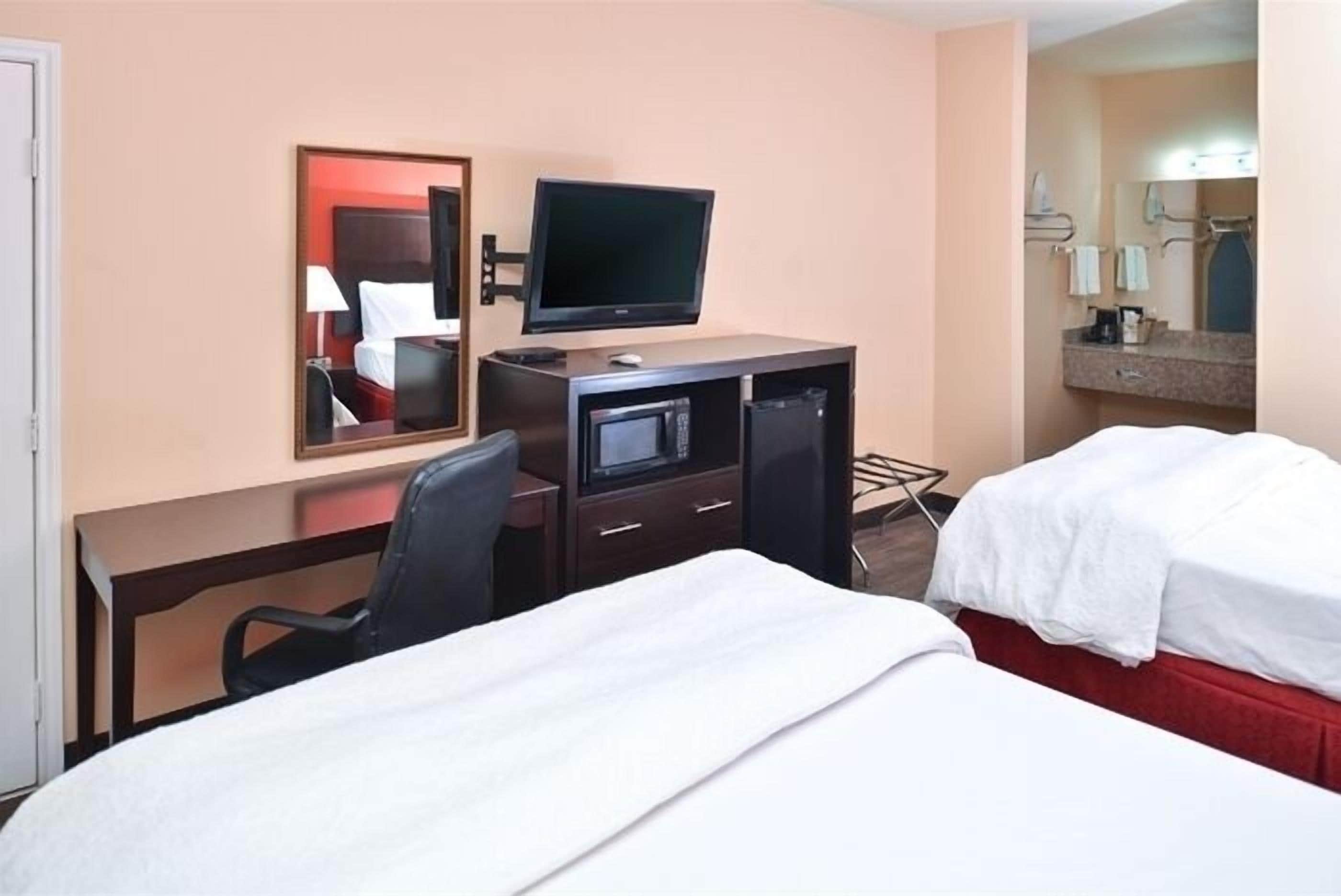 A hotel room with a bed, a desk with a television, a chair, and a mirror.