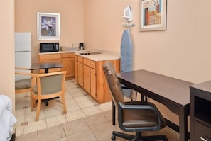 A compact kitchen with wooden cabinets, a microwave, a sink, and a dining area with a chair and table.