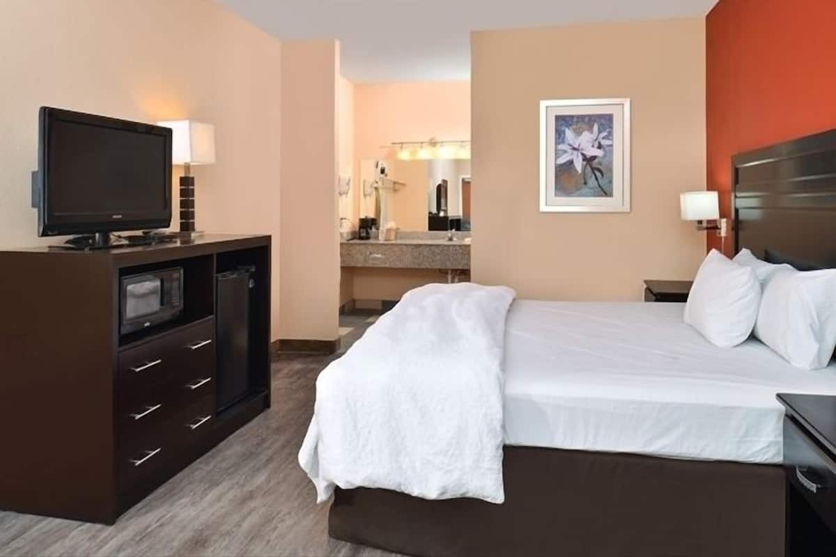 A hotel room with a bed, a TV, a desk, and a bathroom visible in the background.