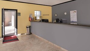 Un área de recepción con escritorio, un basurero, una ventana y un felpudo.