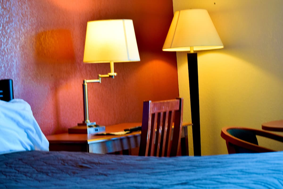A hotel room with a bed, a desk, two lamps, and a chair.