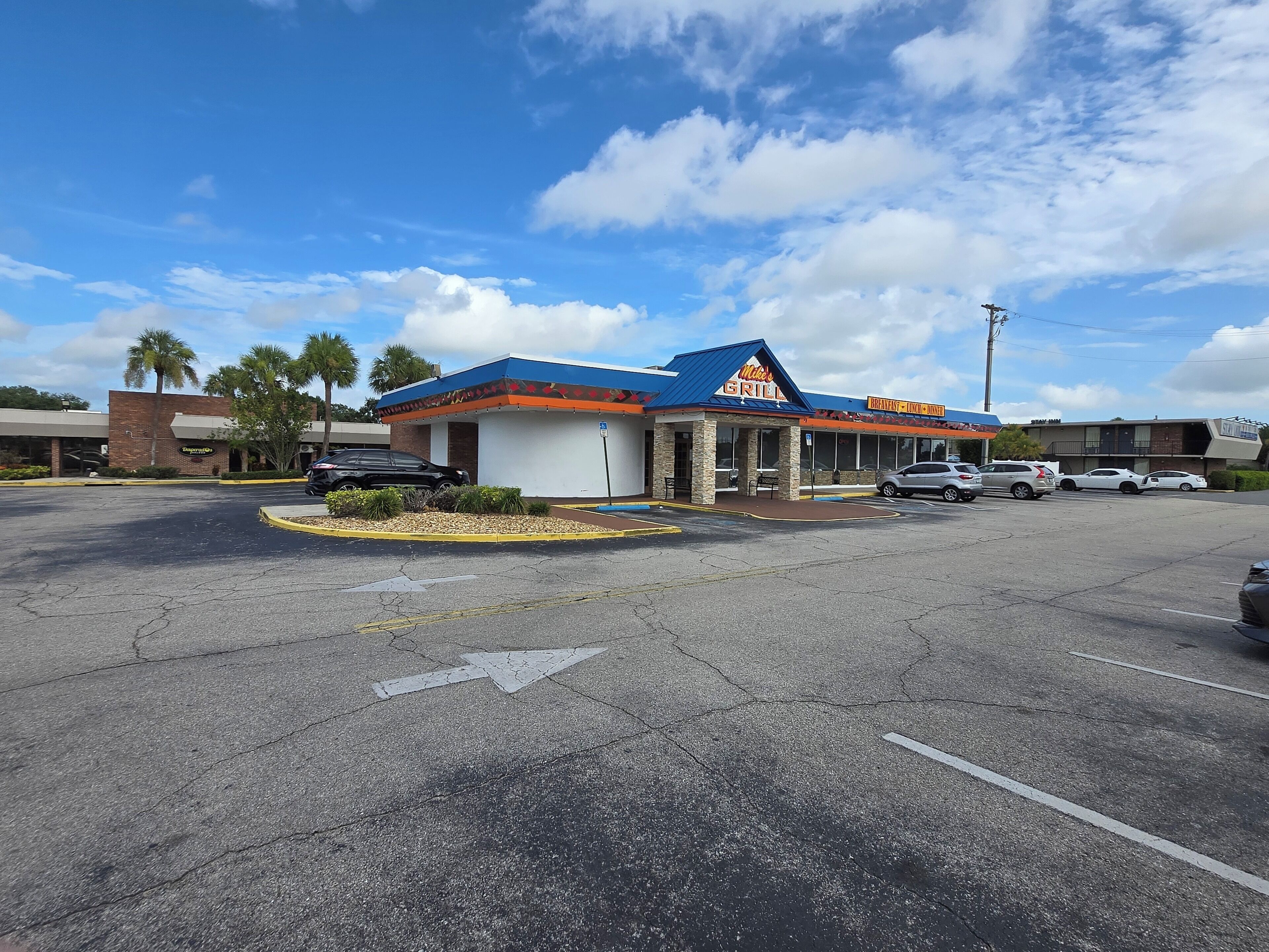 A parking lot with a building labeled "Mike's GRILL" and a sign for "Breakfast - Lunch - Dinner - Waffles".