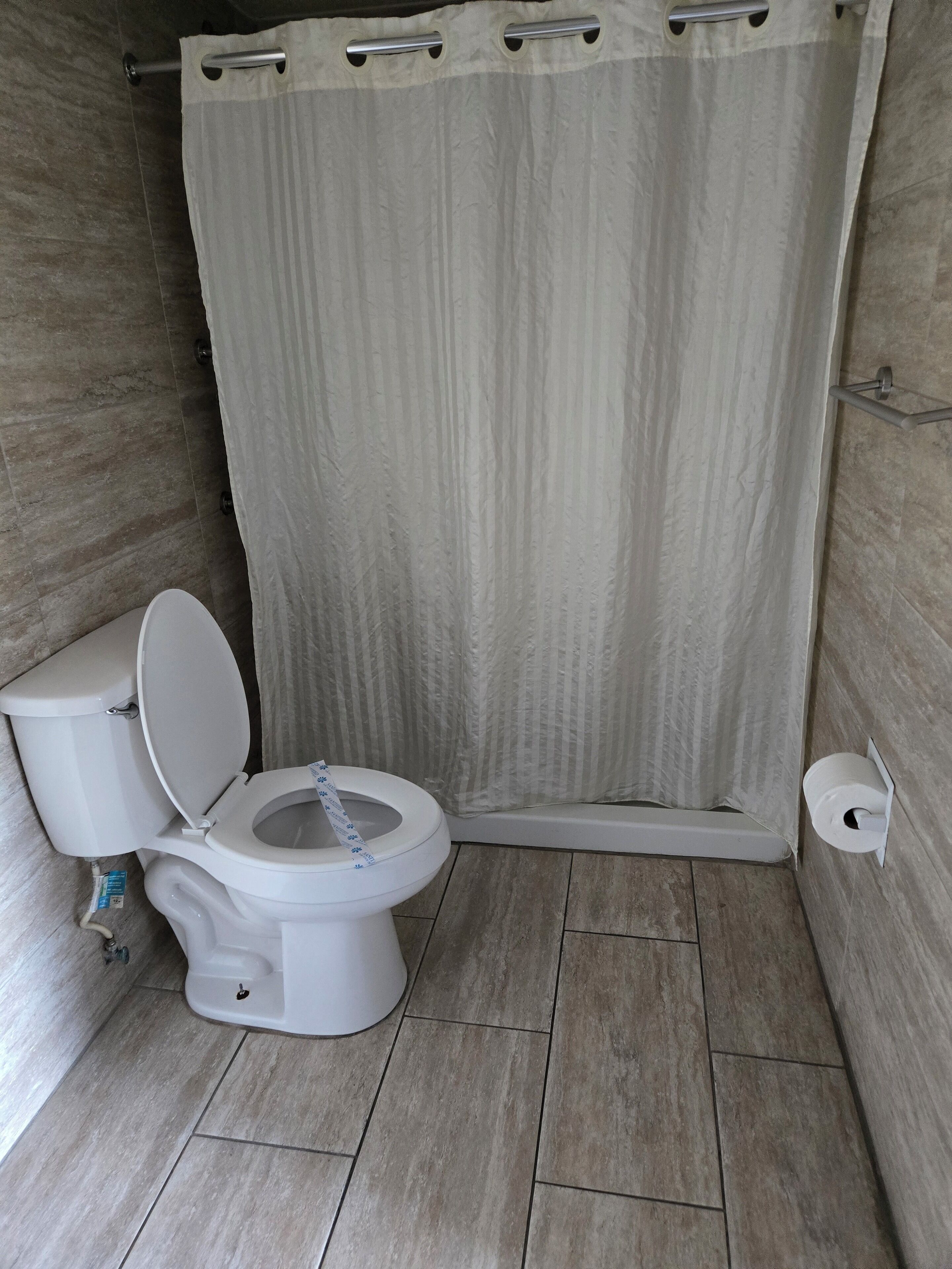 A bathroom with a toilet, shower curtain, and tiled floor.