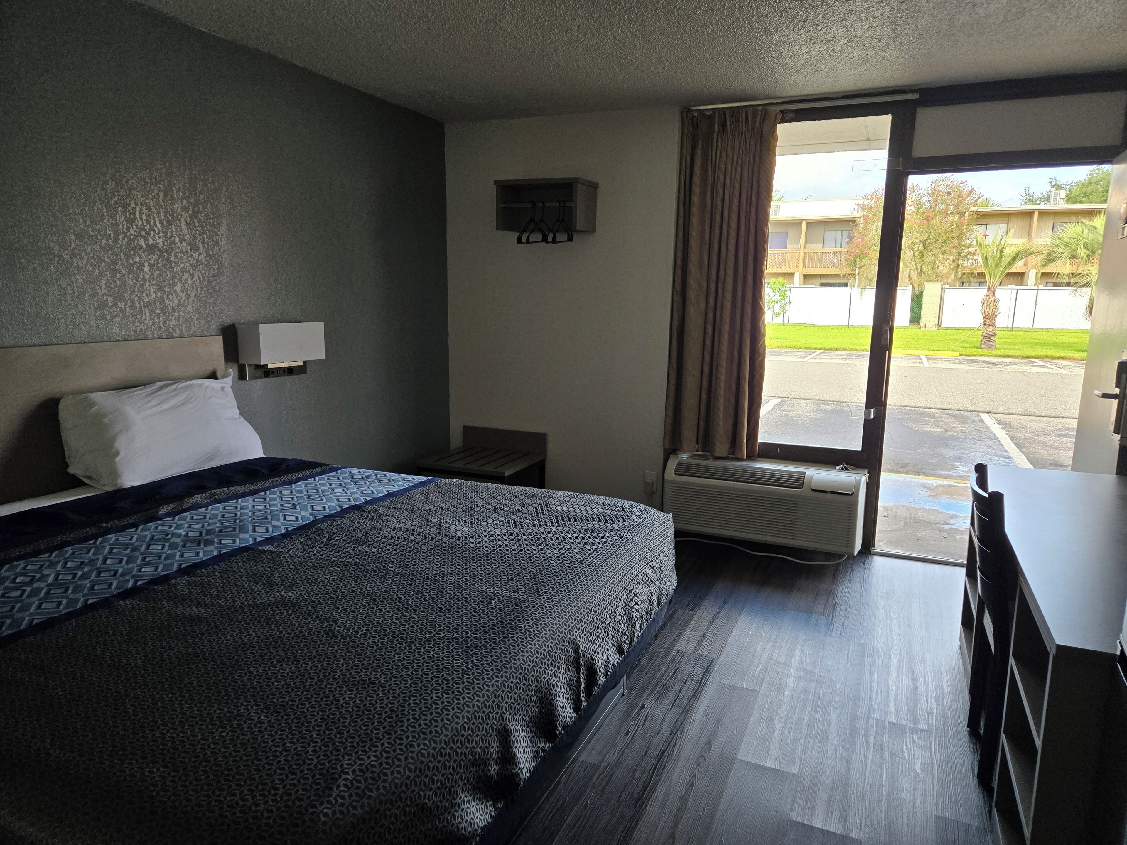 Habitación de hotel con cama, escritorio, silla, ventana con cortinas y aire acondicionado.