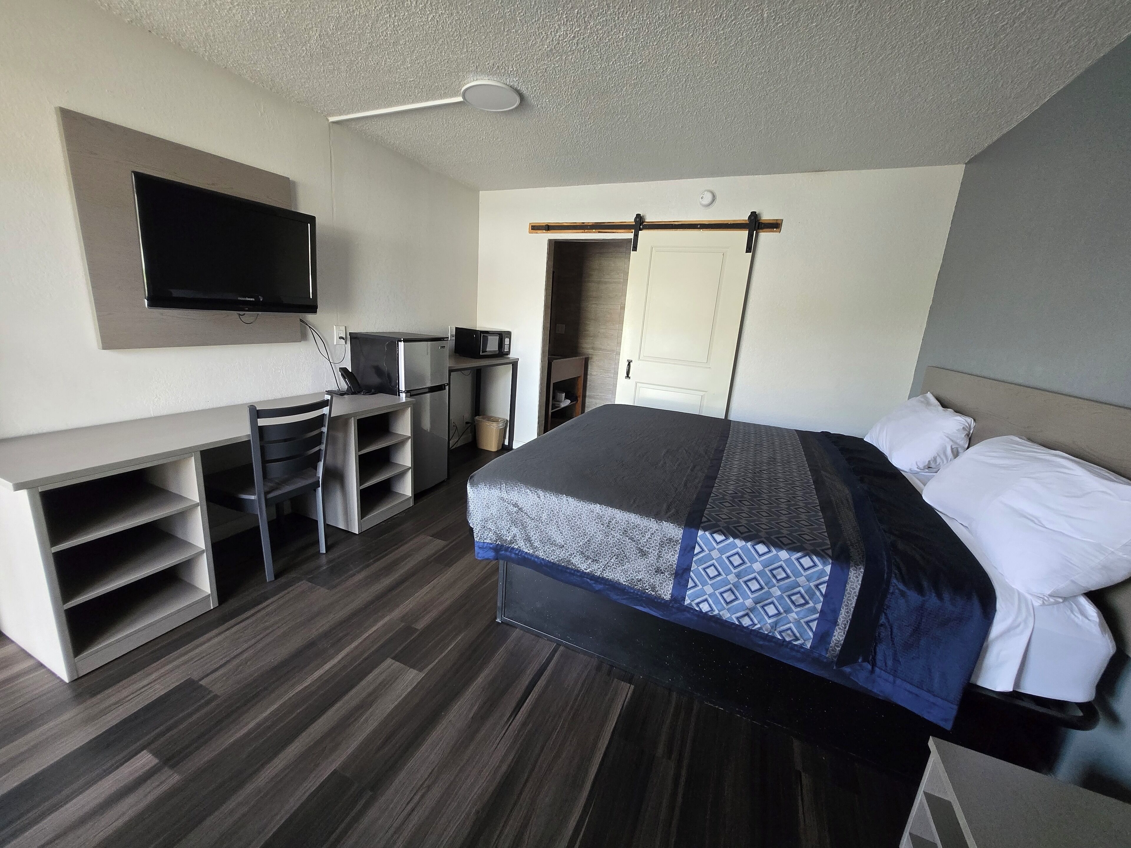 A modern hotel room with a bed, a desk, a television, and a microwave.