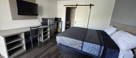 A modern hotel room with a bed, a desk, a television, and a microwave.
