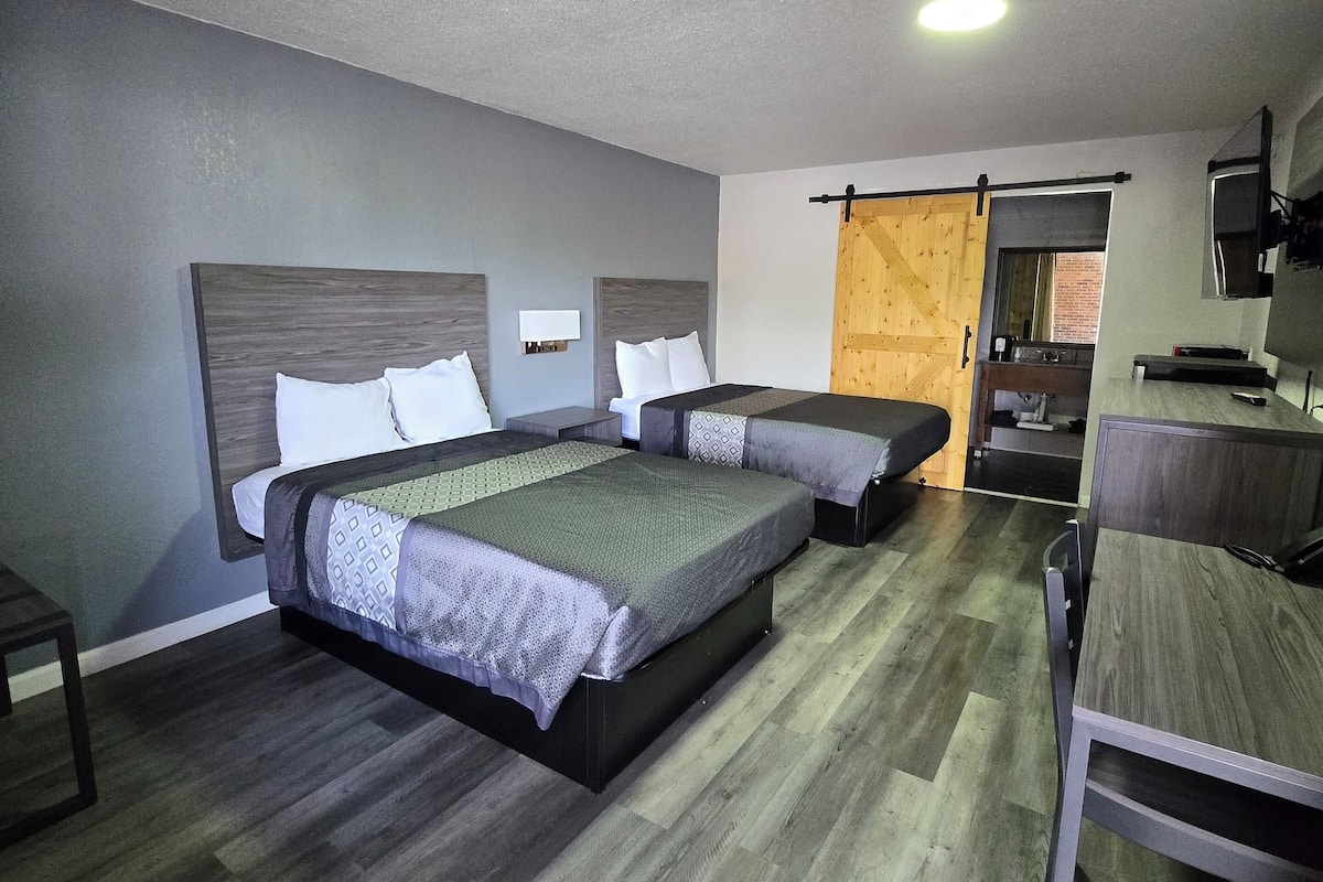 A modern hotel room with two beds, a desk, and a TV.