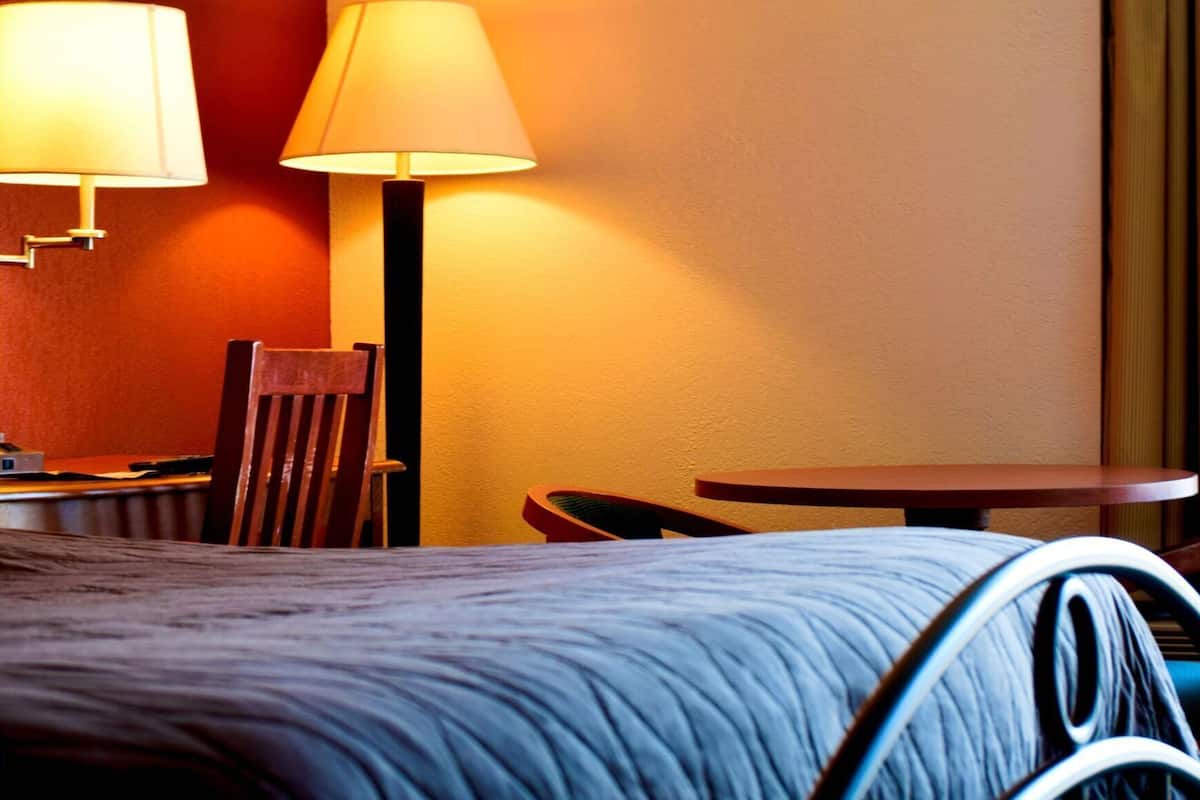 A hotel room with a bed, two lamps, a chair, and a small table.