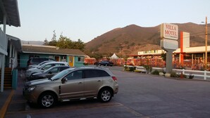 A parking lot with several cars, a motel named 'Villa Motel' with a 'VACANCY' sign, and a 'DAYLIGHT HOME LIGHTING' business in the background. - Villa Motel (San Luis Obispo)