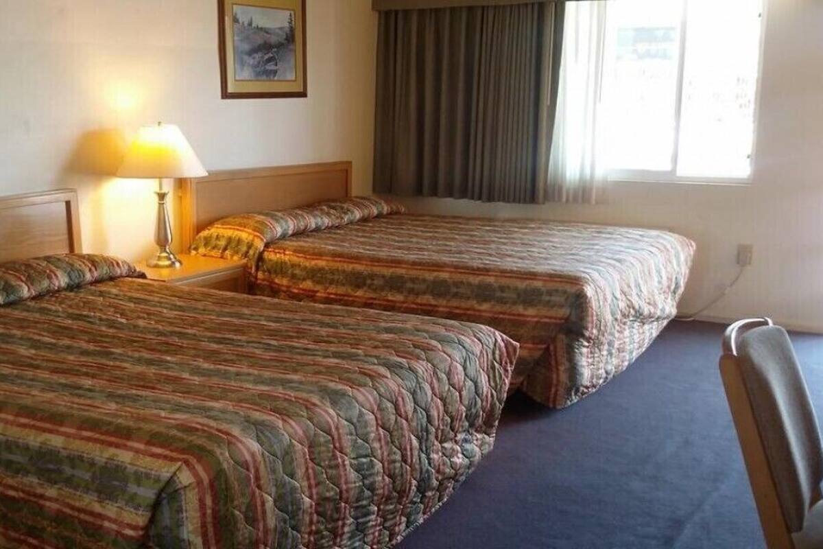 A hotel room with two single beds, a desk, a chair, a lamp, and a window with curtains.