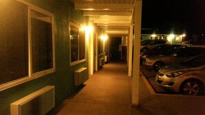 A covered walkway with a row of parked cars on the right and a building with large windows on the left. - Villa Motel (San Luis Obispo)