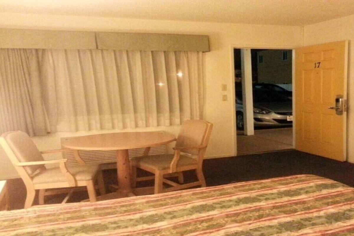 A hotel room with a bed, a TV, a desk with two chairs, and a door leading to a balcony.