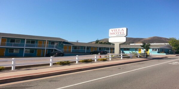 A motel with a sign reading "VILLA MOTEL VACANCY" in front of a two-story building with a blue exterior and a white fence in the foreground. - Villa Motel (San Luis Obispo)