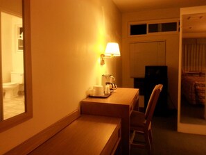 A small, dimly lit room with a wooden table, a chair, a lamp, and a television. - Villa Motel (San Luis Obispo)