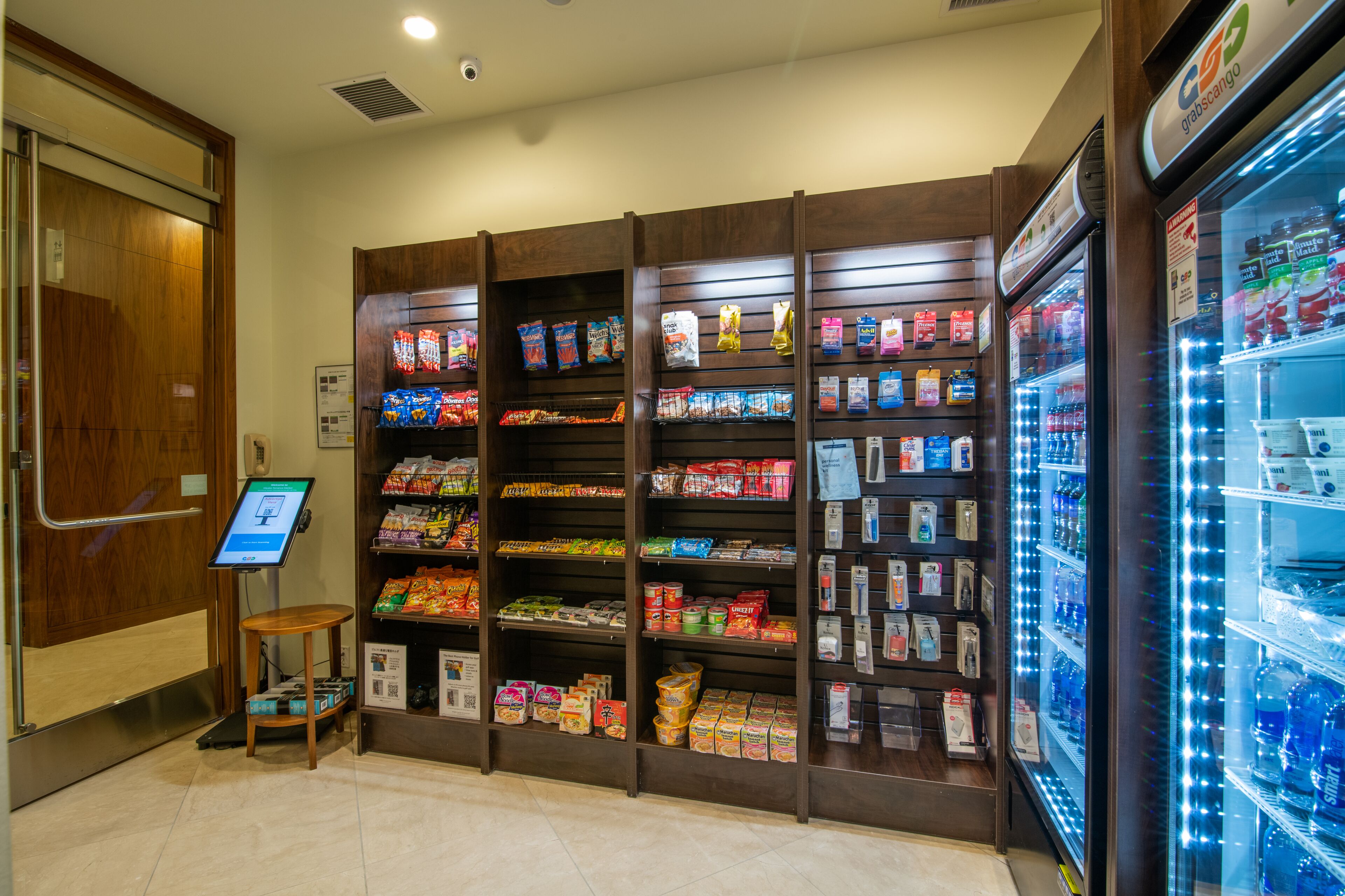 Un kiosque en libre-service doté d’un écran numérique, entouré d’étagères remplies de collations et de boissons.