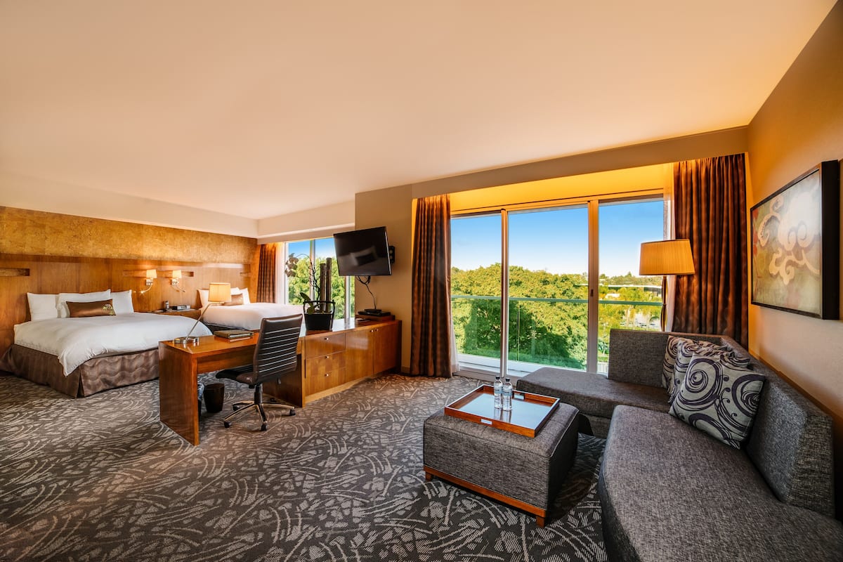 A hotel room with a bed, desk, sofa, and large windows offering a view.