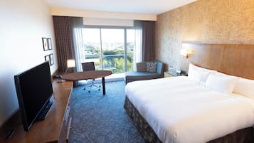 Ein Hotelzimmer mit einem großen Bett, einem Schreibtisch, einem Flachbildfernseher und Blick auf die Stadt durch das Fenster.