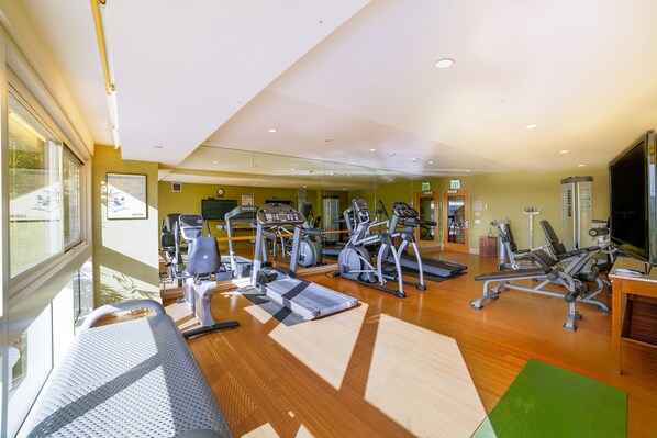 A gym with various exercise equipment, a large mirror, and a television.